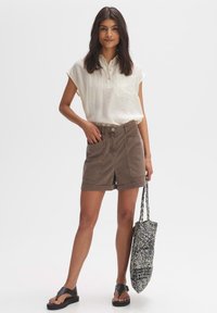 Lichte, off-white collared shirt, bruine denim shorts, zwarte sandalen en een getextureerde blauw-witte geweven tas.