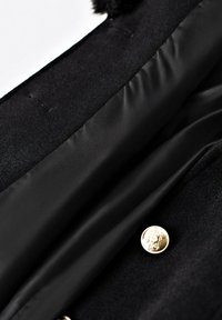 Czarny płaszcz z gładką satynową podszewką, złotymi guzikami i miękką fakturą na zewnętrznej tkaninie. Zbliżenie na kołnierz i podszewkę.