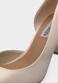 Gros plan sur des chaussures à talons hauts beiges avec une texture lisse et une étiquette de marque visible à l'intérieur d'une chaussure.