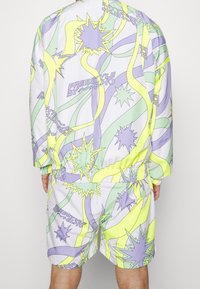 Kolorowy dres z abstrakcyjnym wzorem w jasnofioletowym, żółtym i zielonym kolorze, z elastycznym pasem i mankietami, wykonany z gładkiej tkaniny.