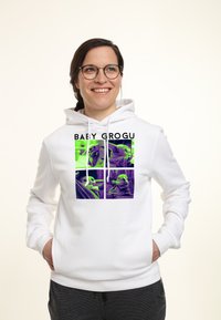 Hoodie blanc avec un imprimé graphique comportant quatre images d'un personnage dans des tons verts et violets, intitulé "BABY GROGU". Tissu doux, poche kangourou.