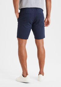 Pantaloni corti blu navy in cotone misto, con tasche posteriori e taglio dritto, abbinati a sneakers bianche.