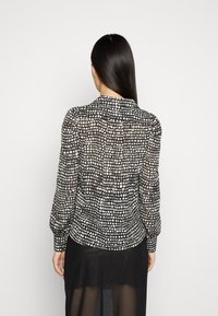 Black and white polka dot blouse featuring long sleeves, a collar, and a slightly sheer fabric. The design includes gathered details at the back.