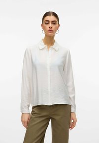 Blusa bianca a maniche lunghe con finitura testurizzata, chiusura a bottoni frontale e colletto. Presenta dettagli sottili nei polsini e nell'orlo.