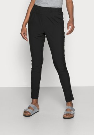 Pantalons noirs fuselés avec une taille élastique, dotés de poches latérales et d'une texture lisse. Assortis à des sandales grises avec un détail de boucle.