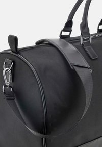 Borsa a duffle nera con tessuto testurizzato, dotata di manici in pelle liscia, una clip laterale e una silhouette morbida e arrotondata.