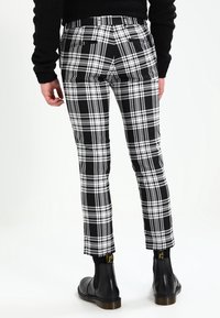 Černobílé kostkované kalhoty se slim fit, s pružným pasem a dvěma zadními kapsami, nošené s černými chelsea botami.