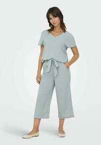 Ljusgrön tvådelad outfit med en kortärmad V-ringad topp och högmidjade, vida byxor med en knytbälte. Slät textur.