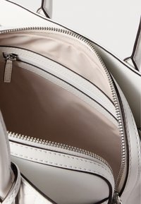 Εσωτερικό λευκής τσάντας με λείο, ανοιχτό ύφασμα επένδυσης. Διαθέτει μία τσέπη με φερμουάρ και δύο ανοιχτές θήκες. Ασημί μεταλλικά στοιχεία.