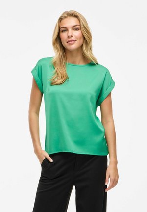 Grøn kortærmet bluse med rund hals, glat tekstur og op-rullede ærmer, parret med sorte bukser. Simpelt, moderne design.