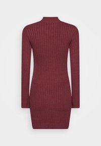 Ribbad stickad klänning i djupt vinröd, med lång ärm och hög halsringning. Materialet visar strukturerade vertikala ränder.