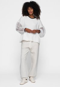 Hvid oversized top med gennemsigtige pufærmer, parret med lysegrå sweatpants med snor. Hvide træningssko fuldender udseendet.
