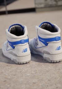 Adidași albi cu glezna înaltă, cu accente albastre, având un superior din piele texturată, guler căptușit și logo-ul vizibil al brandului pe toc și pe lateral.