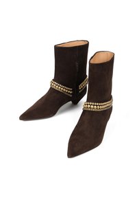 Brązowe zamszowe botki za kostkę z wąskim noskiem, z złotą klamrą z ćwiekami wokół kostki oraz zamkiem błyskawicznym z boku.