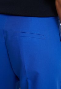 Jasnoniebieskie spodnie o gładkiej fakturze, z prostym wzorem tylnej kieszeni i czystym, dopasowanym krojem.