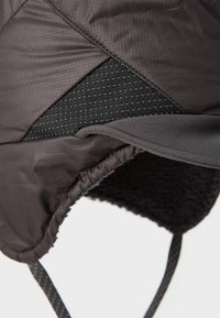 Chapeau isolé noir avec un extérieur matelassé, un panneau en maille texturé et une doublure en polaire douce. Il dispose de sangles ajustables pour un ajustement sécurisé.