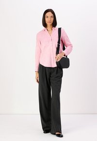 Light pink button-up shirt with a textured pattern, paired with dark wide-leg trousers. Black crossbody bag with embossed logo and black flats.