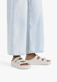 Sandali platform bianchi con tre cinturini regolabili e suola spessa e testurizzata, indossati con jeans a gamba larga blu chiaro.