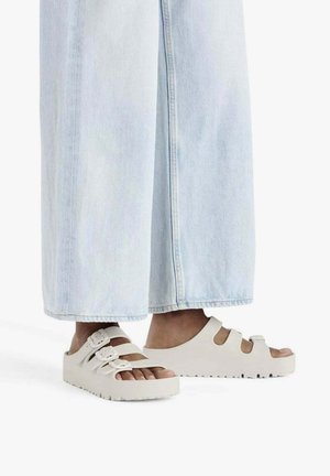 Sandali platform bianchi con tre cinturini regolabili e suola spessa e testurizzata, indossati con jeans a gamba larga blu chiaro.