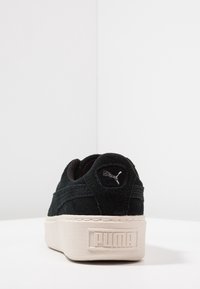 Černé semišové tenisky s krémovou gumovou podešví. Mají strukturovaný povrch, polstrovaný límec a stříbrné logo Puma na patě.