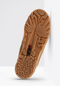 Semelle de chaussure en caoutchouc marron, présentant un motif dentelé avec des accents texturés et un logo de marque noir et rouge près du centre.