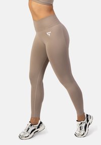 Béžové legíny s vysokým pásom vyrobené z elastického materiálu, s hladkou textúrou, bočnými švami a malým bielym logom na páse.