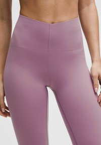 Kergedest lilla kõrge vöökohaga retuusid, millel on sile tekstuur ja õmblusteta disain, mille külgedel on tagasihoidlikud õmblused.