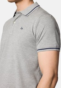 Szara koszulka polo z kołnierzykiem w niebieskie akcenty, dwoma guzikami oraz małym logo na klatce piersiowej. Krótkie rękawy z ribbowanymi mankietami.