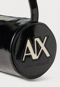Juodas lakinės odos apvalus rankinukas su apvalia baze, su baltu logotipu "AX" ir "ARMANI EXCHANGE" įspaustu priekyje.