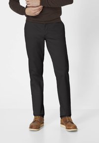 Schwarze gerade geschnittene Hosen mit glatter Textur, ausgestattet mit normalen Taschen und einem Reißverschluss, kombiniert mit braunen Schnürstiefeln.