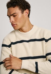 Maglione lavorato a maglia color crema con strisce orizzontali blu navy, scollo rotondo, tessuto strutturato e polsini a coste.