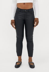 Fekete műbőr nadrág slim fit fazonnal, el�ülső zsebekkel, cipzáras záródással és gombbal. A modellen fekete, pöttyös lapos cipők vannak.