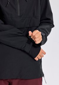 Giacca a pullover nera con colletto alto, coulisse regolabile e polsini in velcro. Texture liscia con design aderente.