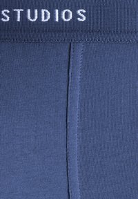Navy blue ribbed fabric with an elastic waistband featuring the word "STUDIOS" in white. Smooth texture and fitted design with visible stitching.