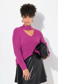 Maglione lavorato a maglia fucsia con collo alto e dettagli a taglio, abbinato a una gonna in pelle nera e a una borsa a pochette nera. Tessuto testurizzato.