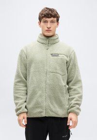 Μπουφάν από φλις σε ανοιχτό πράσινο χρώμα με ψηλό γιακά, φερμουάρ μπροστά και τσέπη στο στήθος. Μαλακή υφή με άνετη εφαρμογή και μακριά μανίκια.