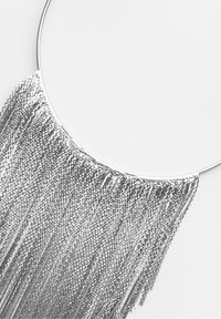 Strieborný vyhláskový náhrdelník s kruhovým kovovým základom a kaskádou strapcov z malých kovových spojok, čo vytvára textúrovaný vzhľad.