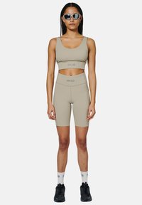 Tan sportbehå och shorts set med "HALO"-logotyp. Slät, elastisk material; tanktop-stil; högmidjade shorts; svarta sneakers.