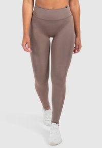 Leggings marroni a vita alta realizzati in tessuto elastico, caratterizzati da una texture liscia e dal design a gamba intera, abbinati a scarpe da ginnastica bianche.