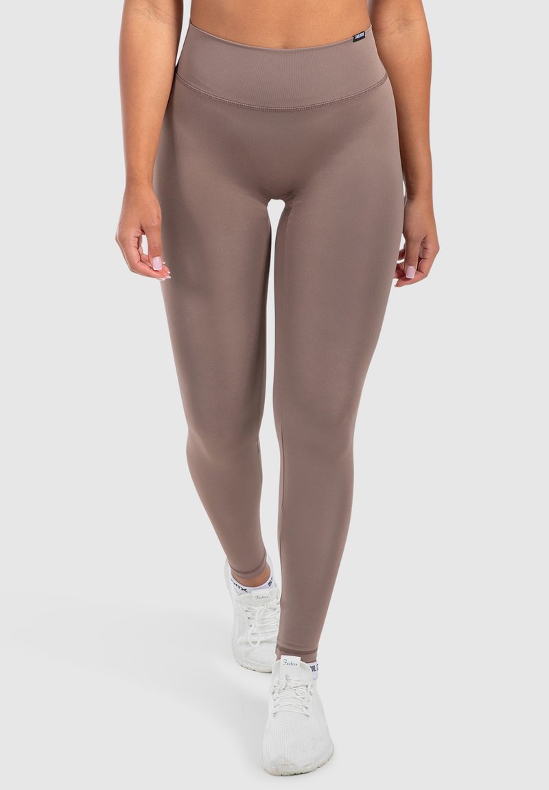 Leggings marroni a vita alta realizzati in tessuto elastico, caratterizzati da una texture liscia e dal design a gamba intera, abbinati a scarpe da ginnastica bianche.