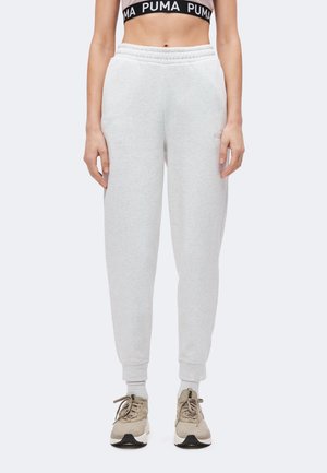 Personne portant un pantalon de survêtement gris clair, des baskets beiges, des chaussettes blanches et un soutien-gorge de sport noir avec le texte "PUMA" sur la bande.