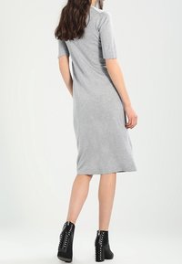 Robe en jersey grise à manches courtes, silhouette droite, longueur genou. Associée à des bottines noires cloutées. Design minimaliste.