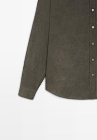 Dunkelolivgrünes Hemd mit langen Ärmeln, durchgehender Knopfleiste, einem einzelnen Manschettenknopf und geradem Saum vor weißem Hintergrund.