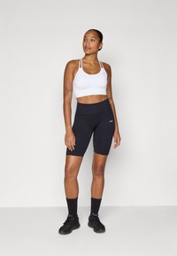 Hvit sports-bh og høyt midje svarte sykkelshorts, begge tettsittende, kombinert med svarte joggesko og ankelsokker, glatt stoff tekstur.