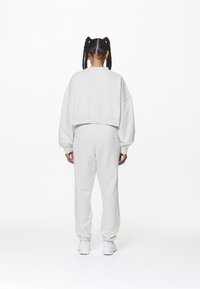 Sudadera blanca recortada con puños elásticos, combinada con joggers blancos a juego y zapatillas blancas, con una textura de tela suave.