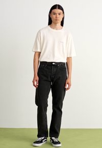 Ljust beige t-shirt med korta ärmar, kombinerad med mörka svarta jeans och svarta Vans sneakers med vita sulor. Enkel och avslappnad klädsel.