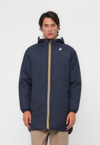 Námornícky modrý parka s bielou kožušinou na kapucni, žltým a oranžovým zipsom a elastickými manžetami. Obsahuje logo na hrudi pre branding.