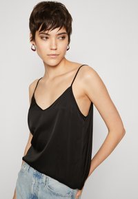 Black satin camisole top with a V-neck and thin straps, featuring a relaxed fit and smooth texture, paired with light blue denim shorts.
