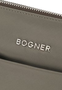 Mörkgrå nylonzippered påse med präglad silver "BOGNER"-logotyp. Slät textur, minimalistisk design och kontrasterande zip-detail.