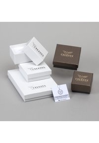 Des boîtes à bijoux blanches et marron avec des logos, empilées à des angles. Un collier pendentif exposé avec une carte d'information à côté des boîtes.
